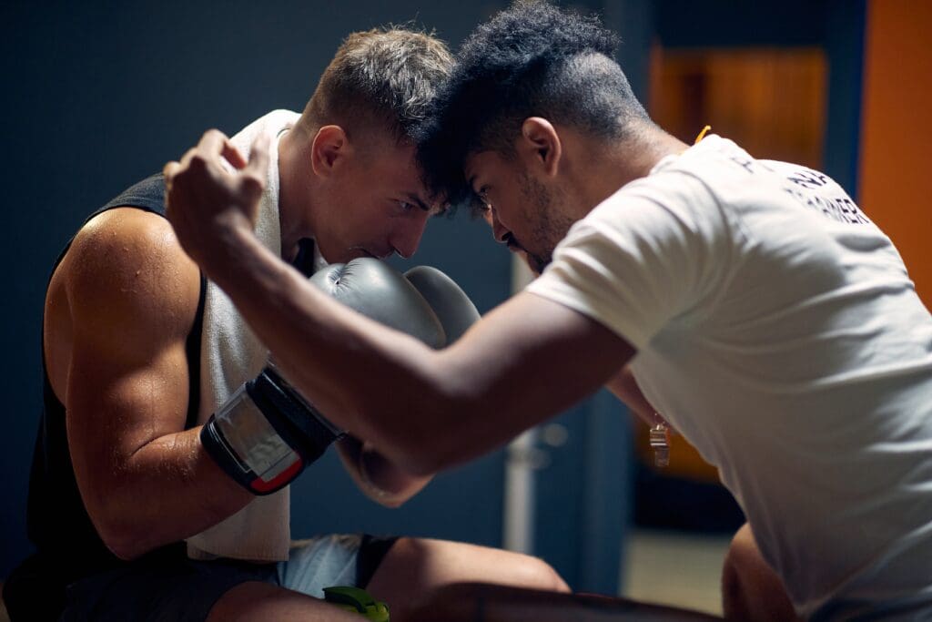 Ein Mann nutzt Methoden der Sportpsychologie, um einen anderen zu motivieren. Beide tragen Sportkleidung, der eine sogar Boxhandschuhe und ein Handtuch um den Nacken.
